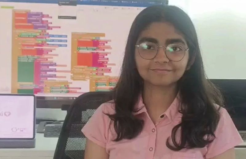Anisha Sharma sitting in front of a monitor filled with App Inventor code blocks.